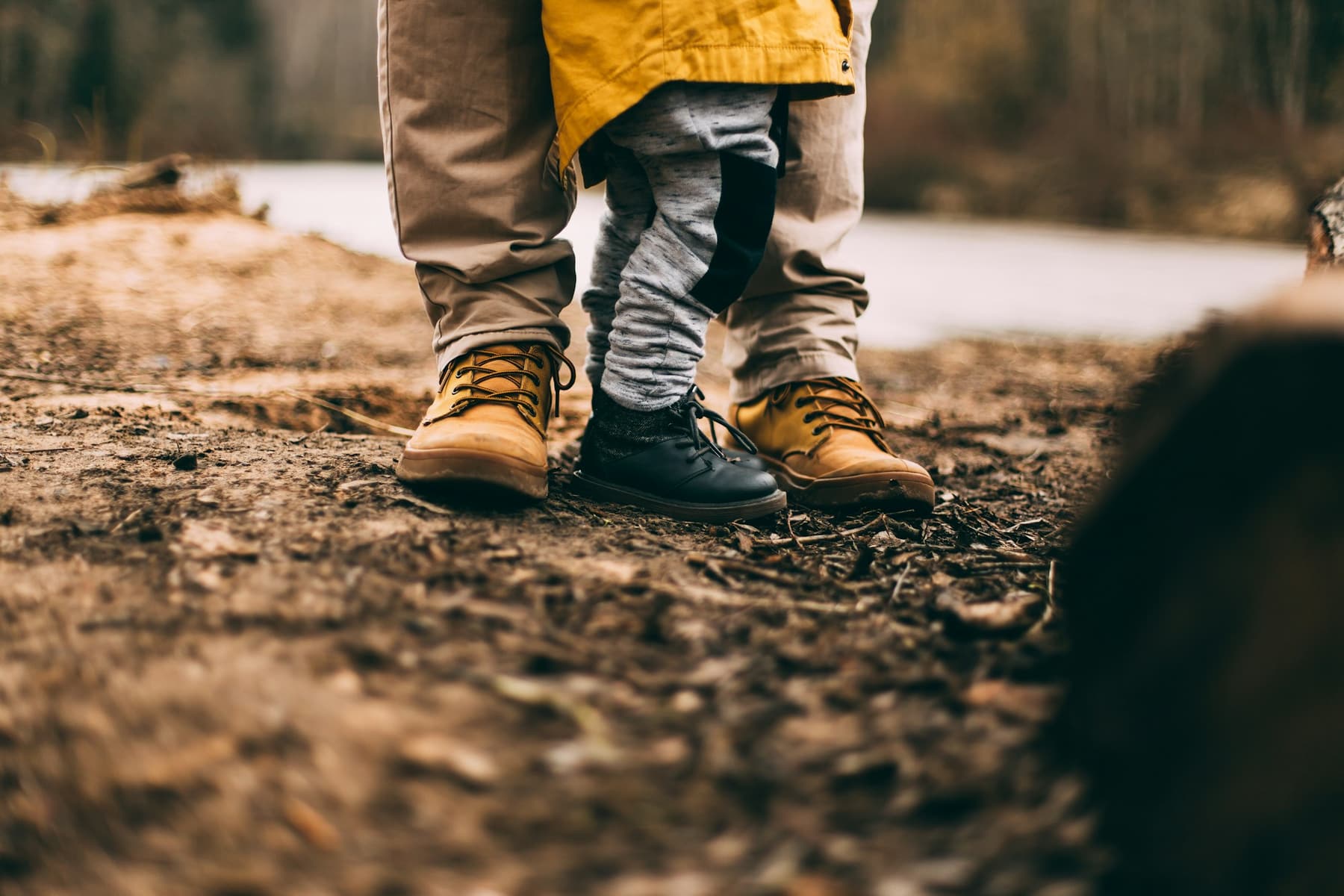 An adult’s and a small child’s boots side by side on a dirt path