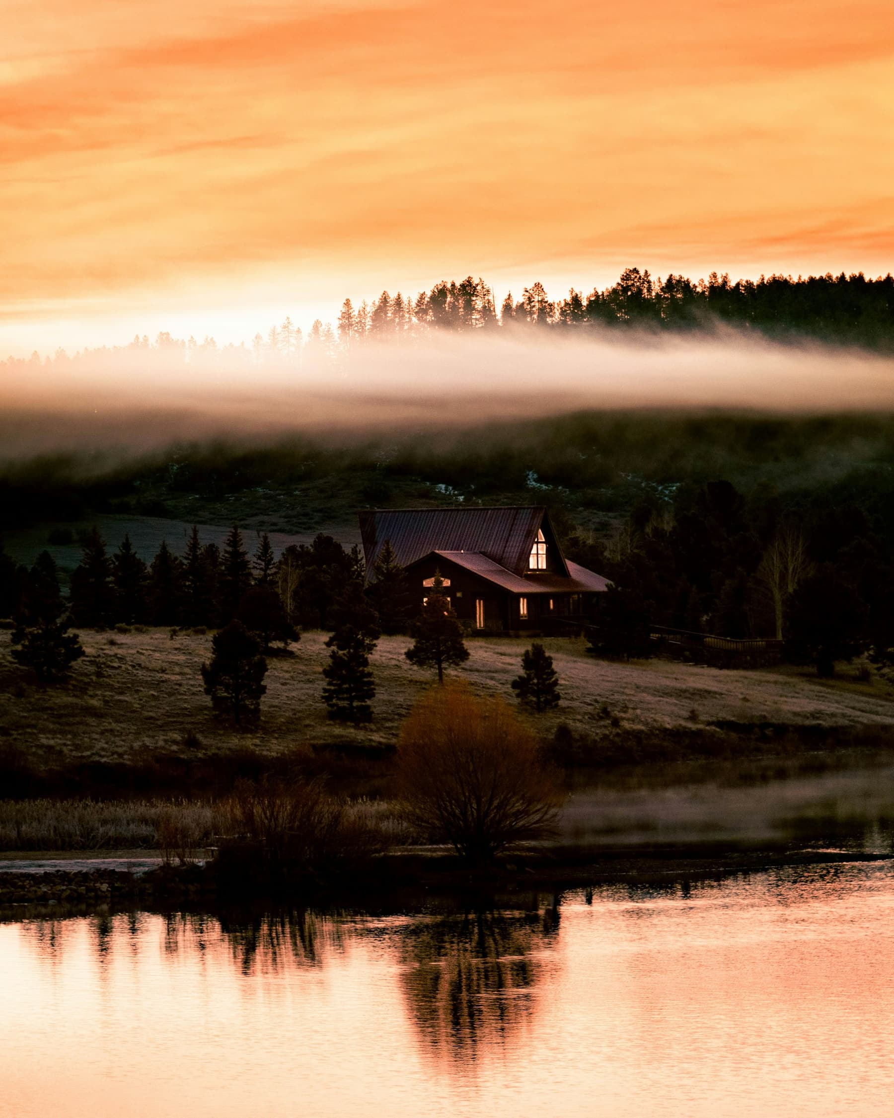 Morning mist over a lake and forest, a house among the trees
