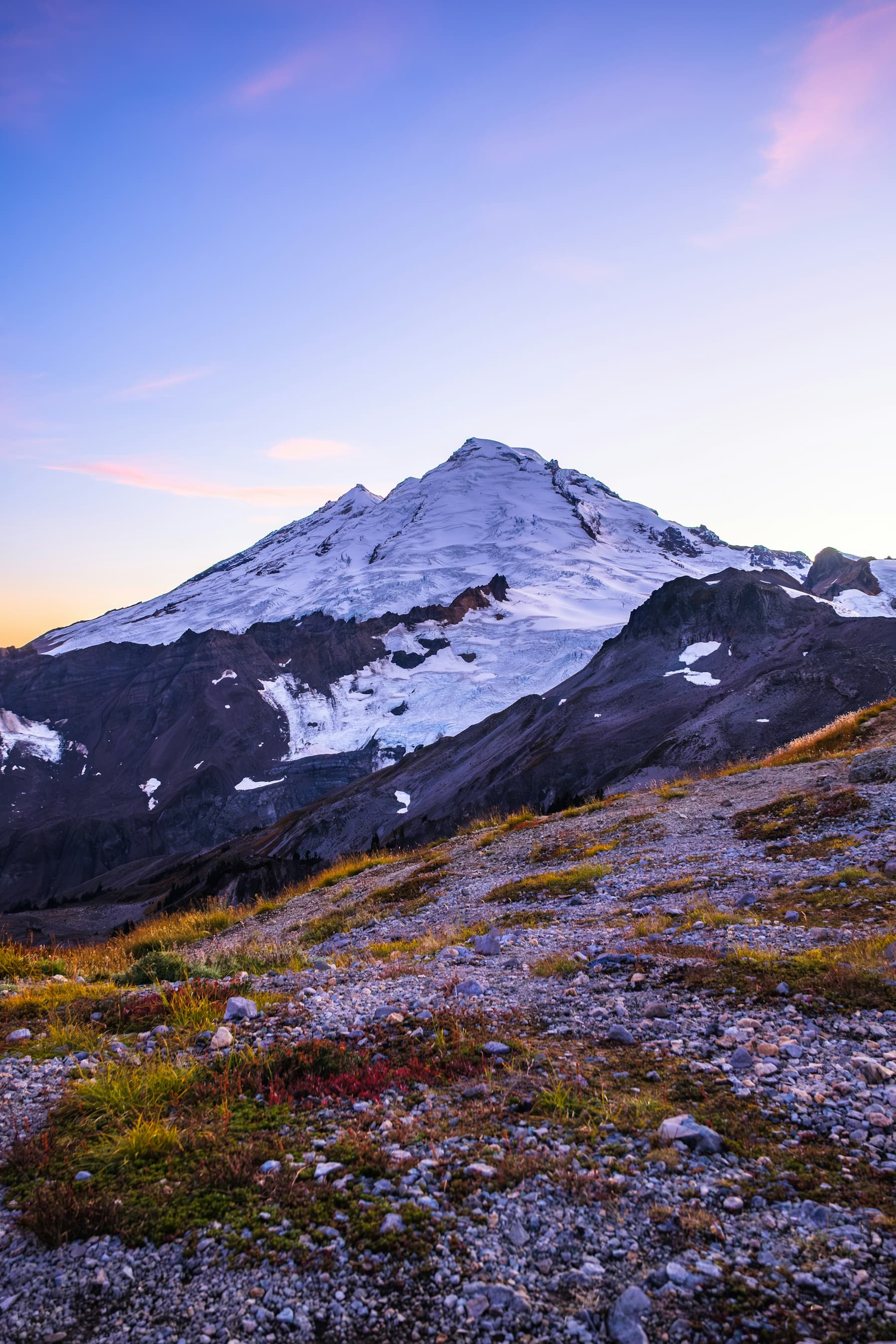 A snow-covered peak at sunrise under a pale purple sky