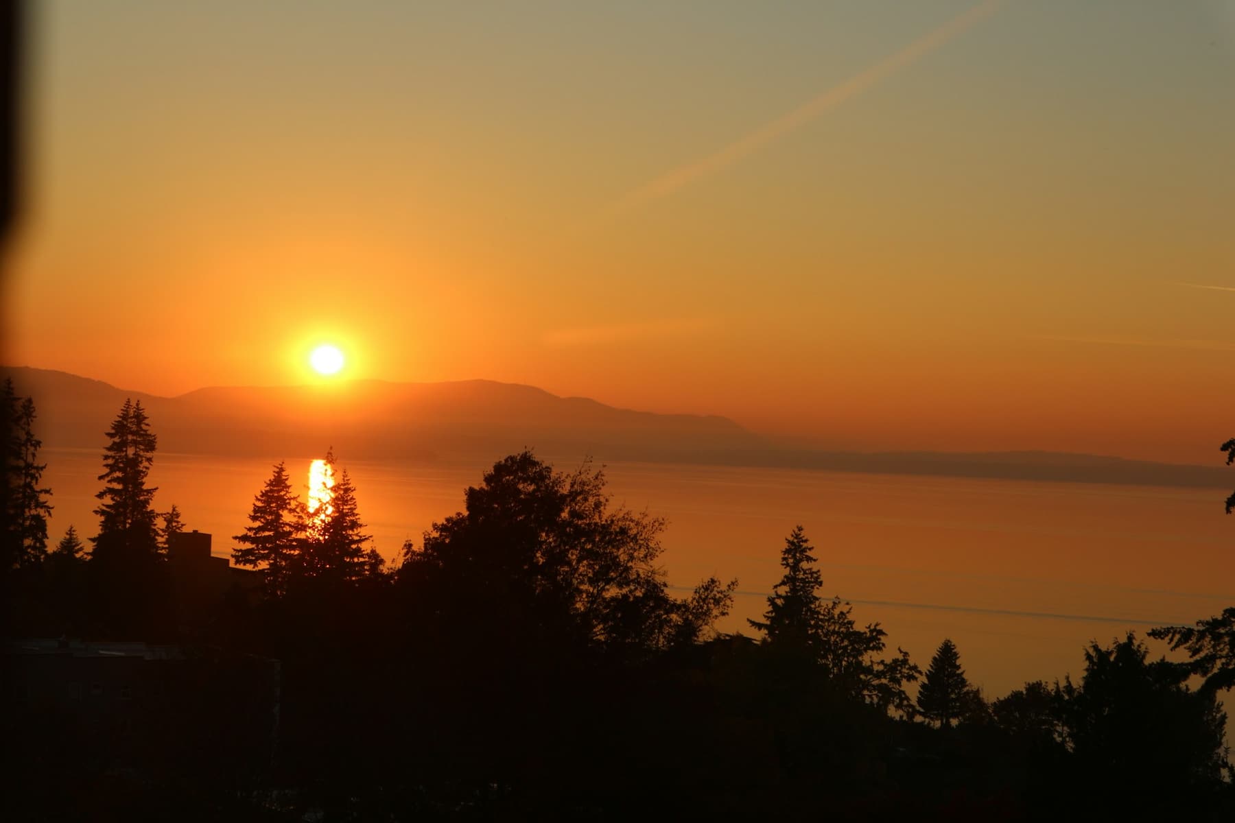 The sun setting over calm water with low mountains on the far shore